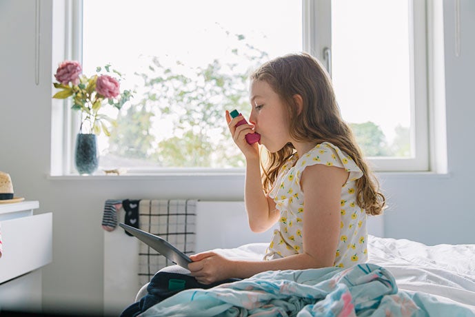 Young girl on bed using asthma inhaler